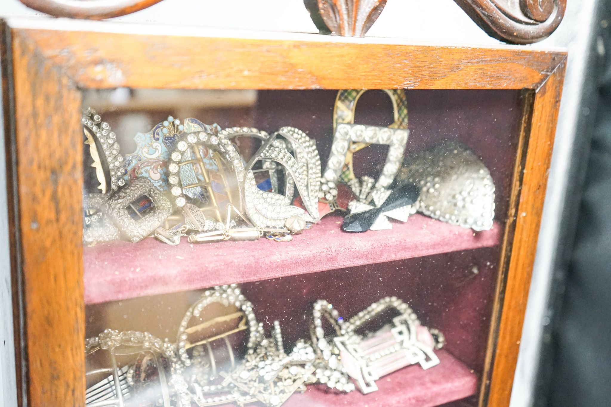A large collection of 19th/20th century paste and enamel belt and shoe buckles and clips, contained in an oak display cabinet. 56cm